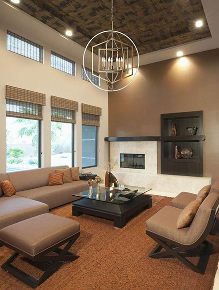 Interior modern living room, with rust colored carpeting, light brown leather furniture with dark wood accents, dark wood glass-topped coffee table in the center of the furniture, white marble fireplace on a brown accent wall with dark wood built-in small bookcase, white second wall with multiple tall windows with rattan shades, brown and black painted ceiling from which hangs an Elk Home Geosphere 12264/7 Midcentury Modern chandelier