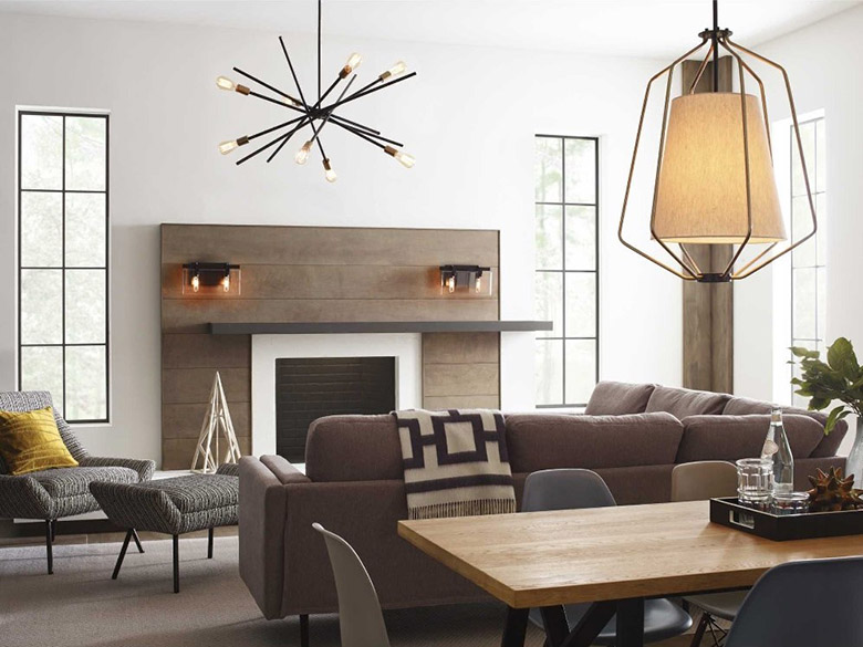  Interior of modern living room with wood floors, brown modern couch and black-and-white striped chair and ottoman, fireplace with modern wood surround with two sconces on either side of the fireplace, white walls with tall, thin black trimmed windows and white ceiling from which hangs one Progress Lighting Astra P400108-020 chandelier