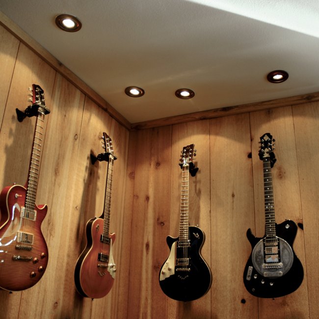 four recessed lights above four guitars hung on a wall