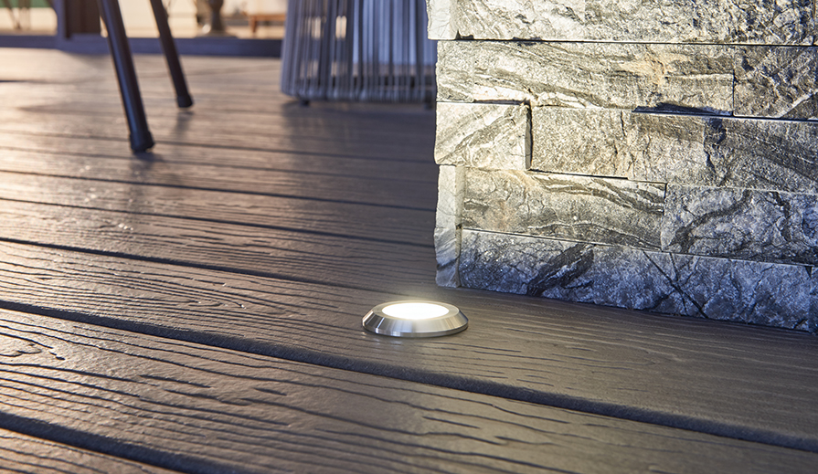 Floor-level porch scene with manufactured wood-look decking, stacked sone corner which is lit up by a Kichler Lighting 16141 mini in-ground light