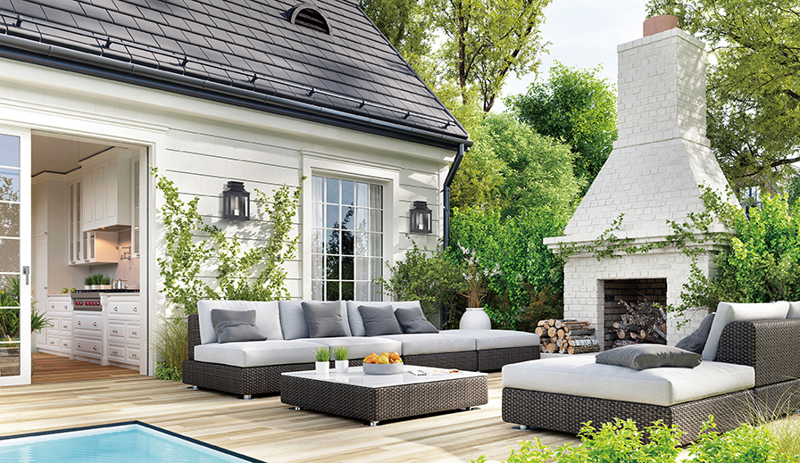  Modern farmhouse outdoor patio scene next to pool, with teak flooring, rattan modern furniture with light gray cushions, massive white brick stand-alone fireplace, cream colored walls on the exterior of the house from which hang two Maxim Lighting Savannah VX 40912CLBO small outdoor wall lights