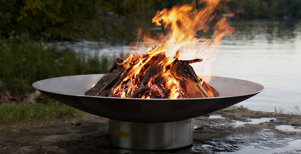 Outdoor shot near a pond, with marshy water and Fire Pit Art BELAVITA34-FPA-MLS120NG fire pit ablaze on the shore