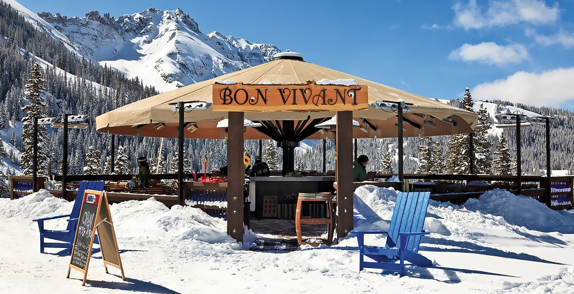 Multiple outdoor patio heaters under covered outdoor dining space with snow covered mountain in background